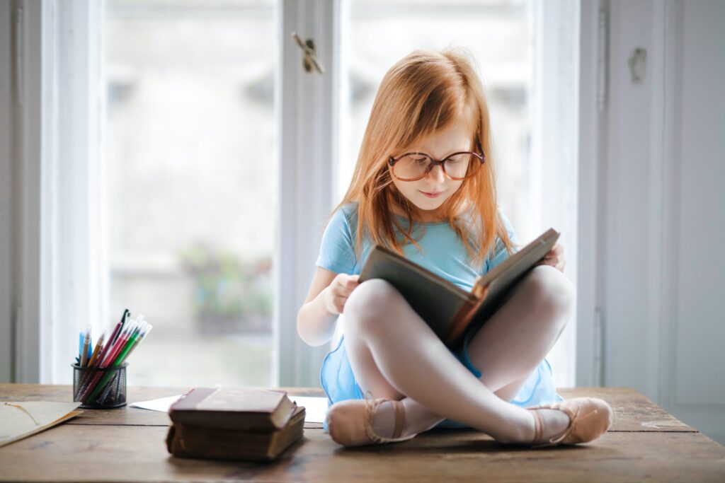 A child wearing large glasses and reading from a book