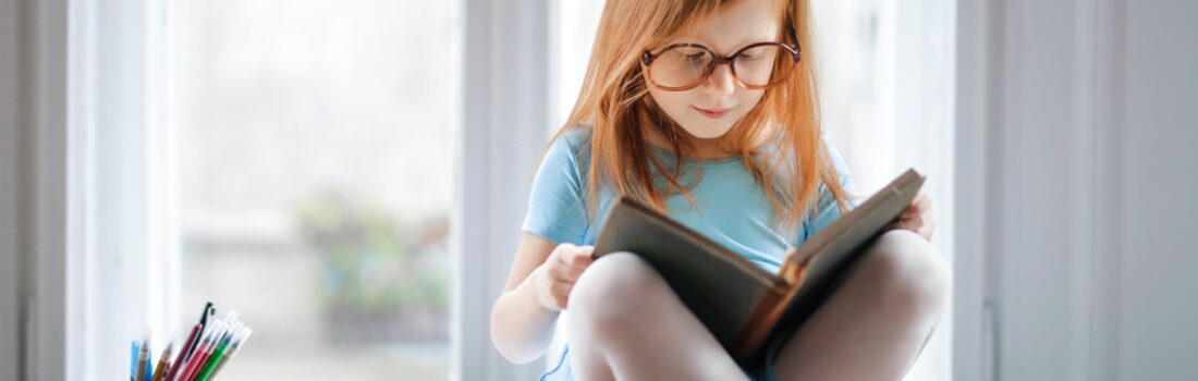A child wearing large glasses and reading from a book