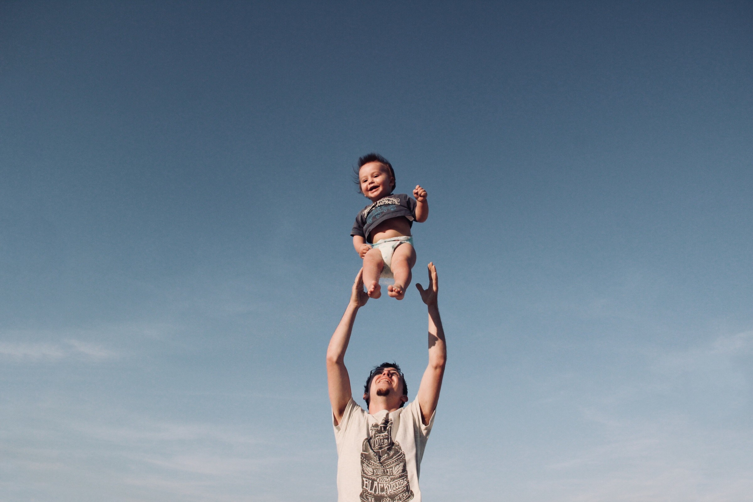 Father tossing up child in the air and smiling.