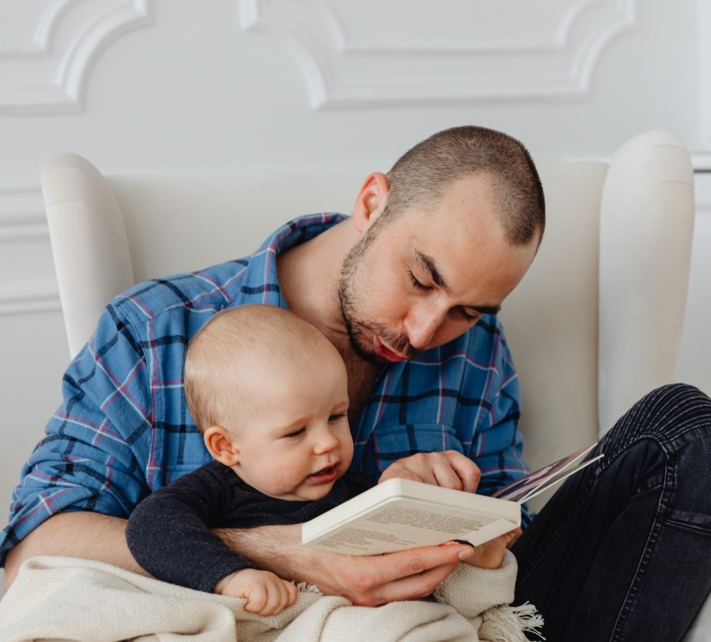 Dad holding book while reading to infant.