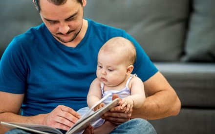 A man reading a book to his baby.