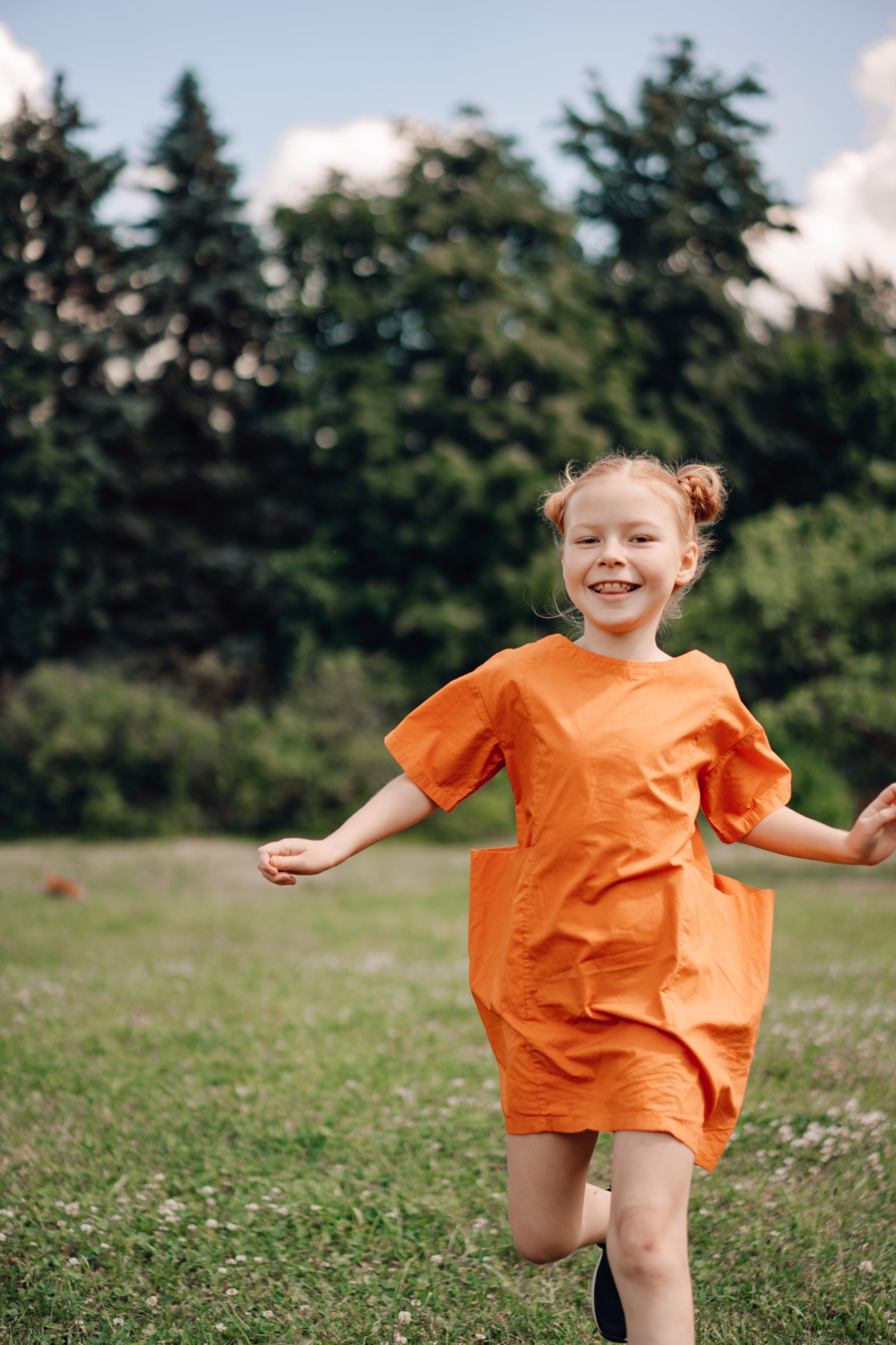 a smiling girl running through a field in an orange dress