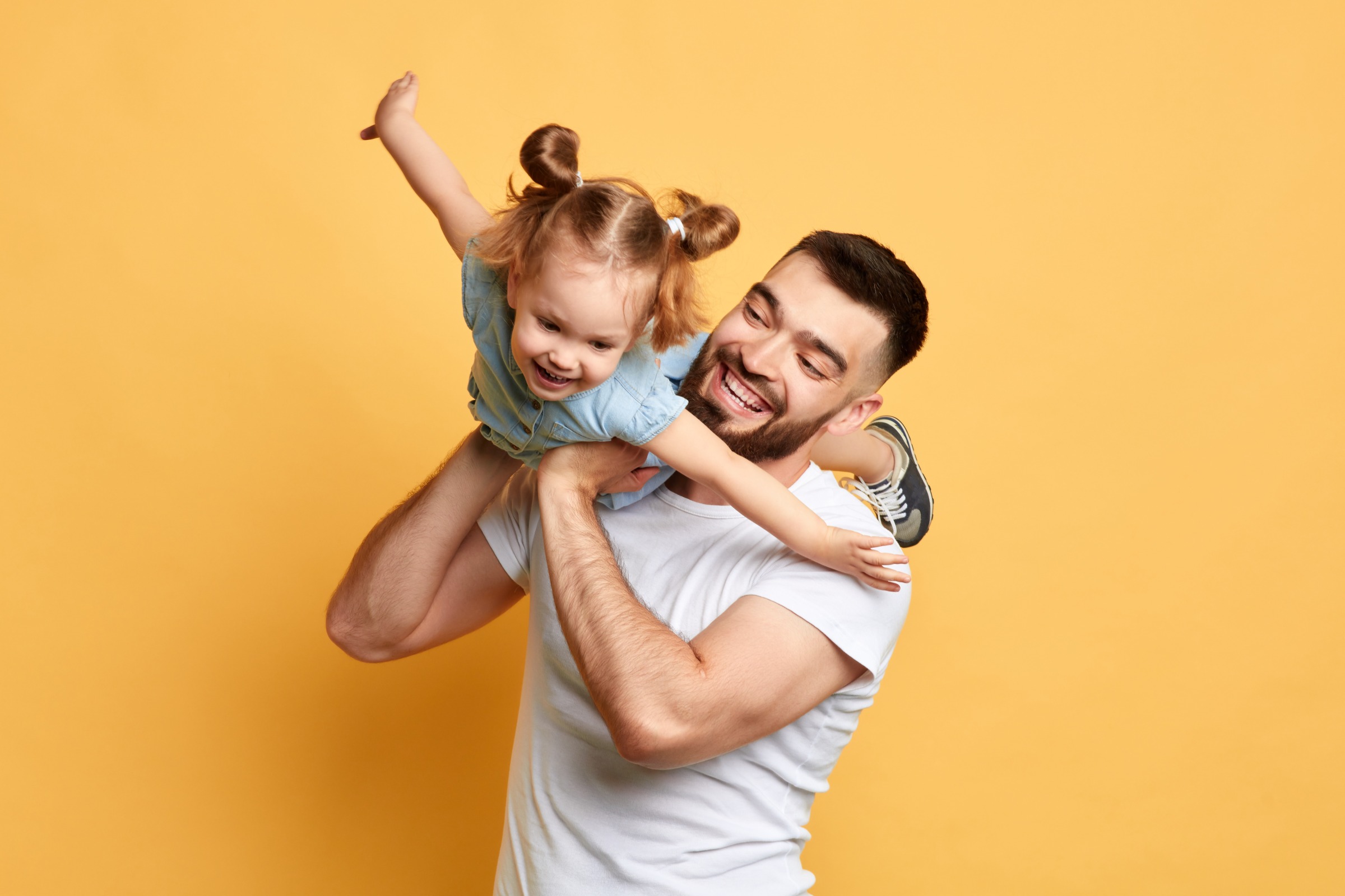 Dad holding his daughter and playing "airplane" by swinging her high in the air.