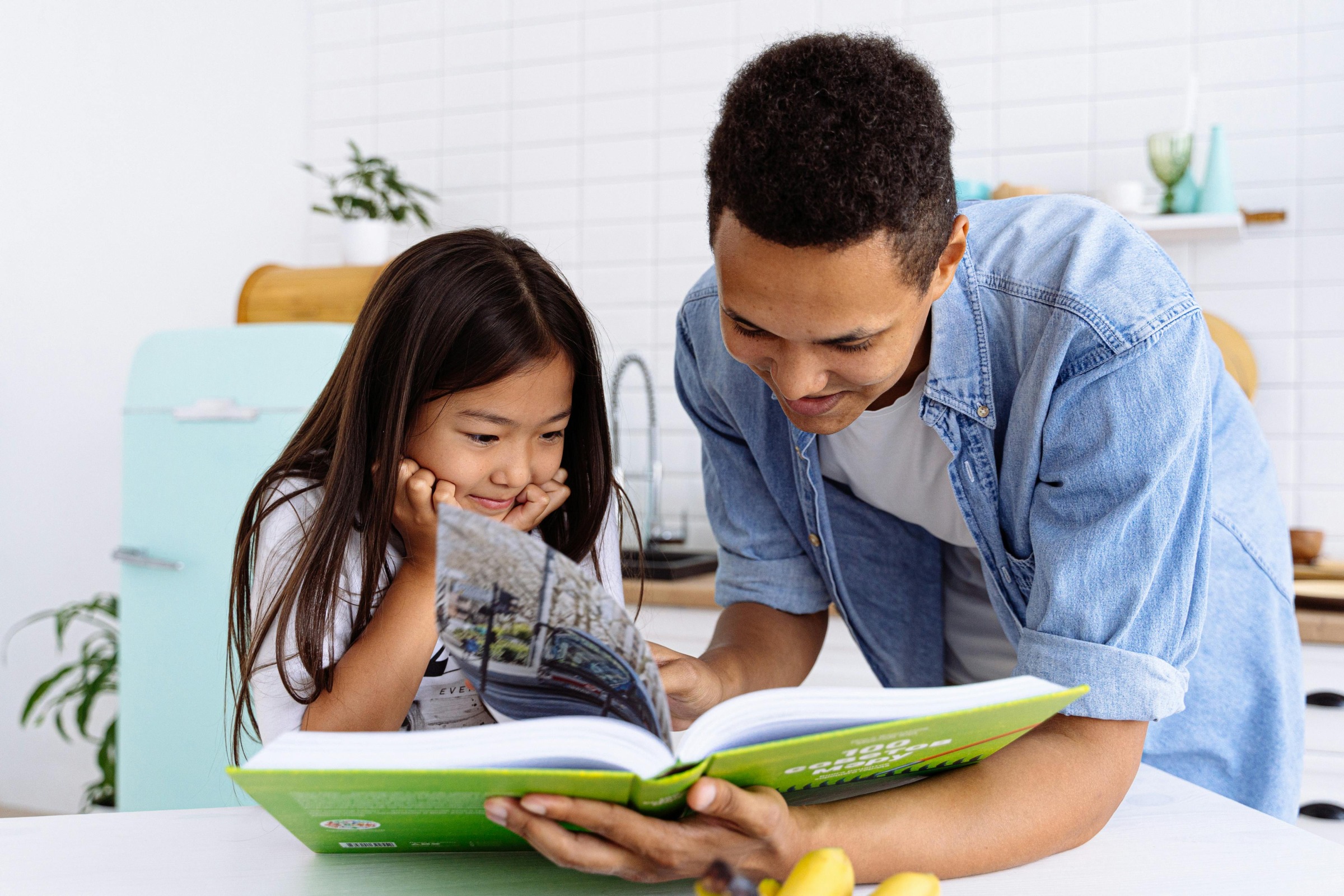 a father and daughter reading a book together in the kitchen