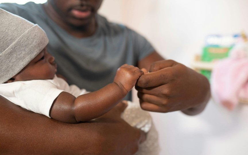 Dad holds infant's hand.