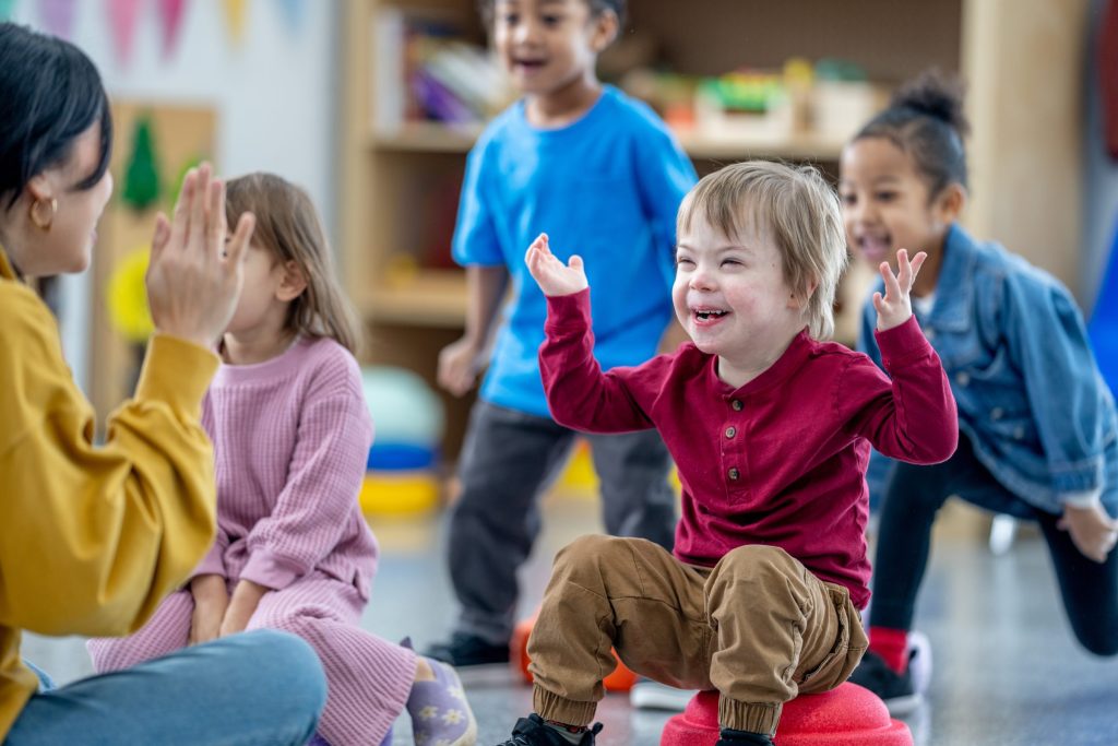 Smiling blond toddler boy who is playing peekaboo with his childcare teacher.