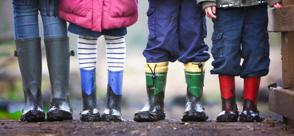 Children wearing muddy rain boots in various colors.