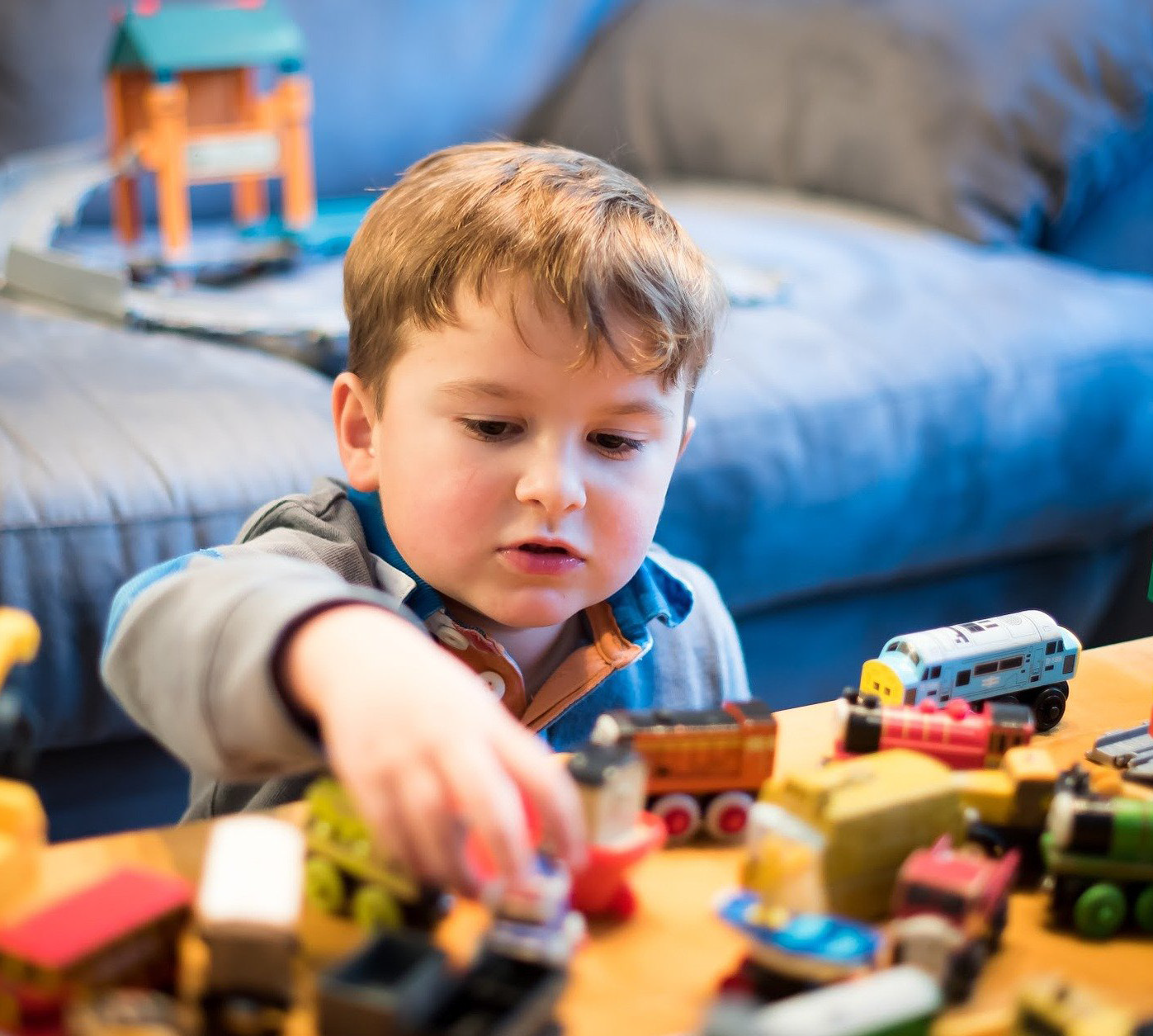 A young child focuses intently while playing with colorful toy trains on a wooden table in a cozy room, creating a scene filled with imagination and joy.