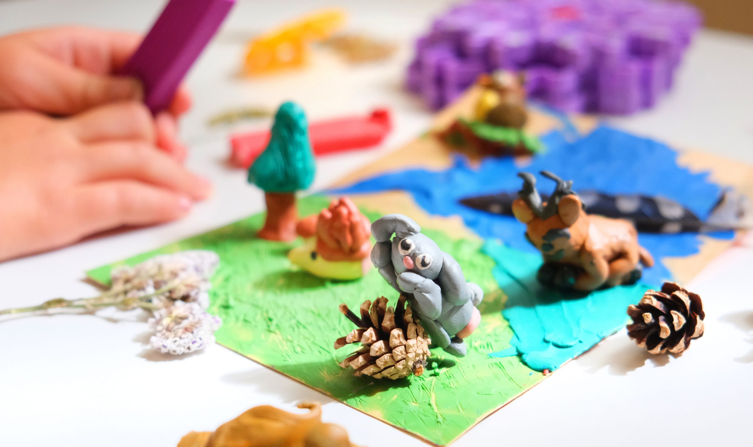Young child's hands playing with small clay animals and pinecones.
