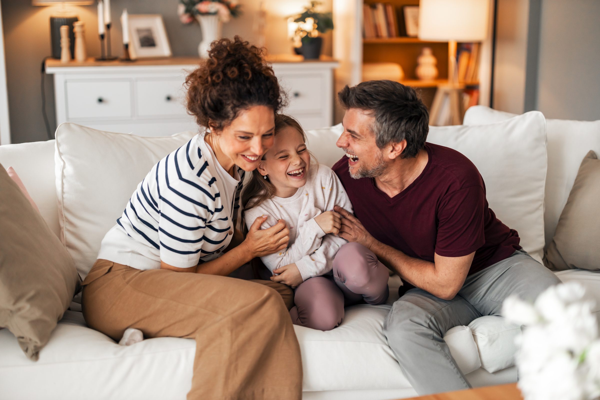 Two parents sitting on a couch and laughing with their daughter.